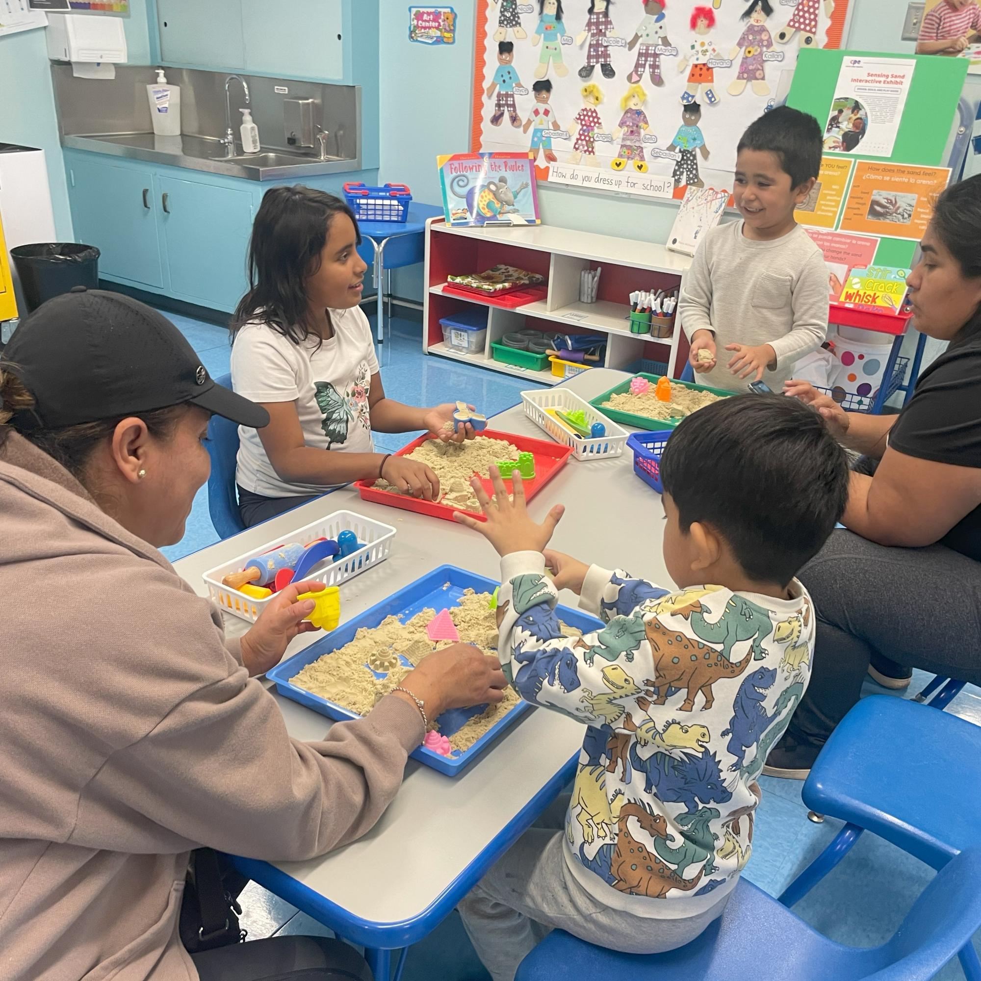 Families play with sand in trays at a table as part of an interactive STEAM exhibit.