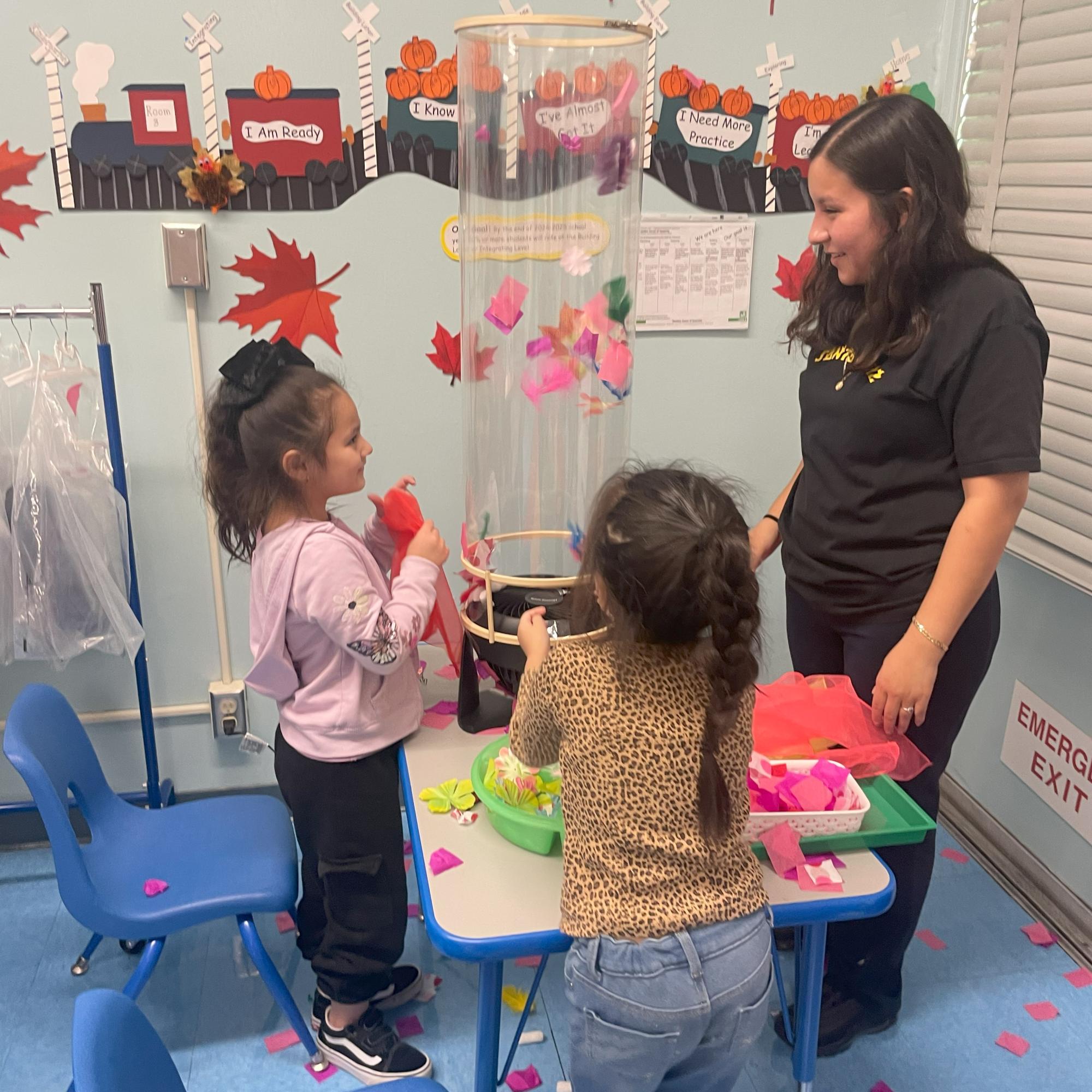 An adult and two children explore a wind tube as part of an interactive STEAM exhibit.