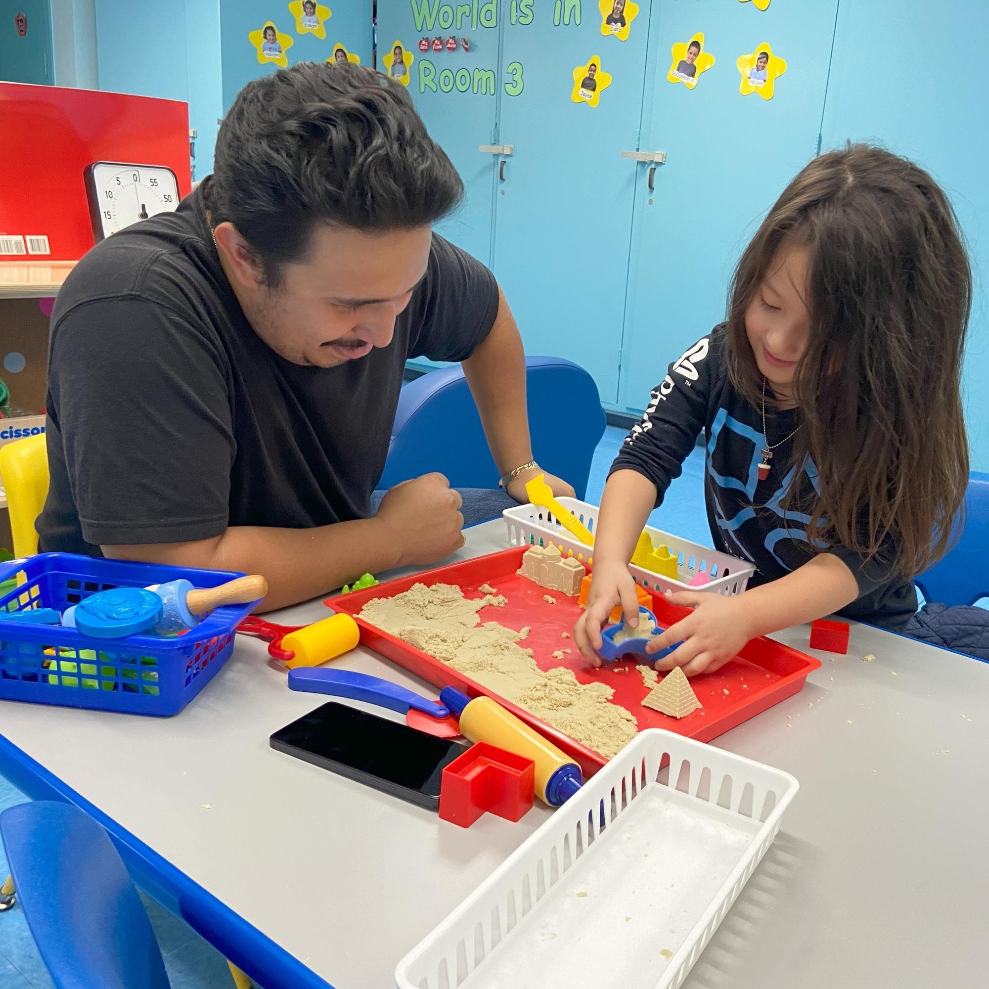 A family plays with sand in a tray at a table as part of an interactive STEAM exhibit.