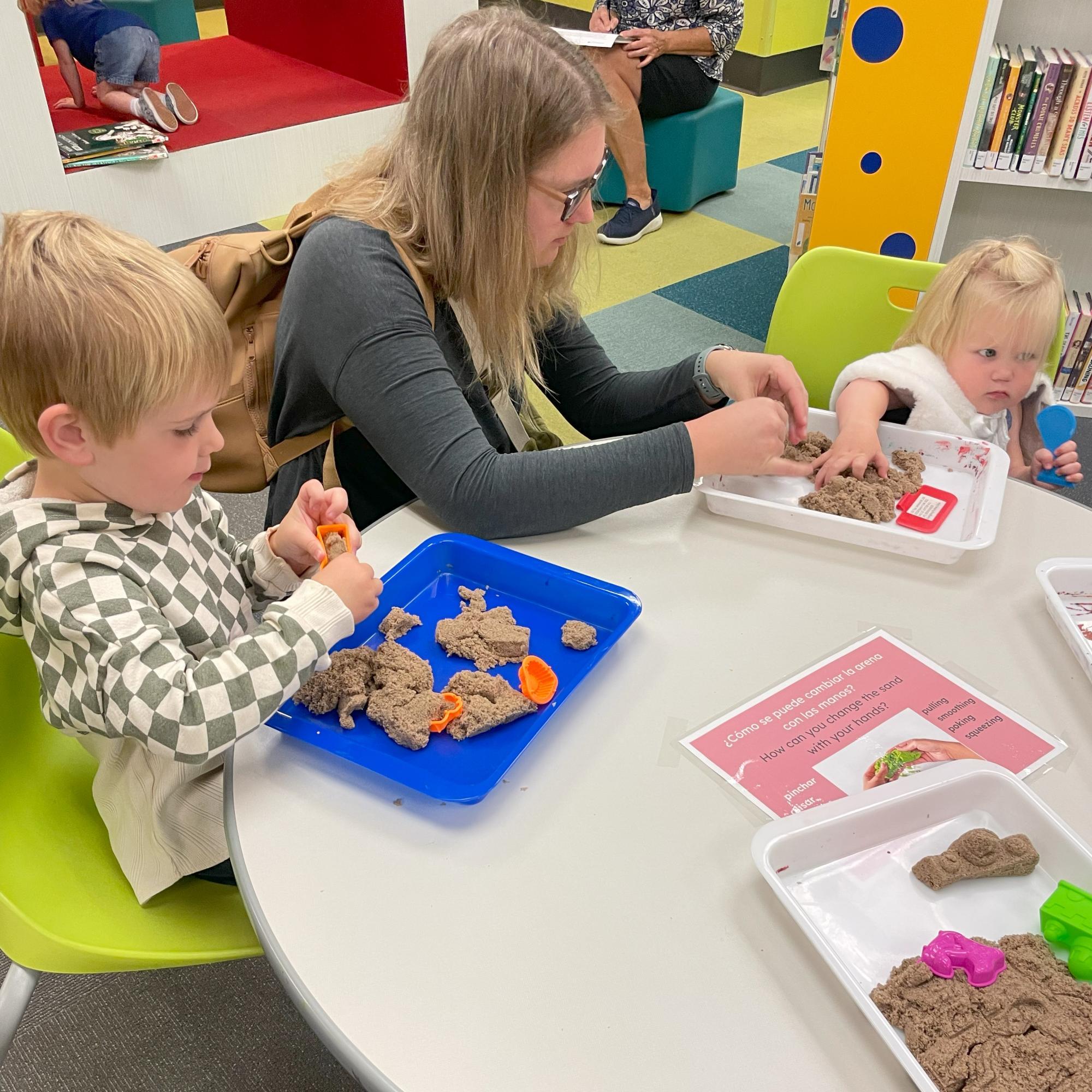 A family plays with sand in trays at a table as part of an interactive STEAM exhibit.